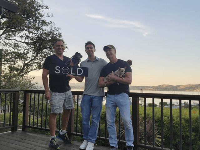 Clients holding a sold sign on a deck at sunset